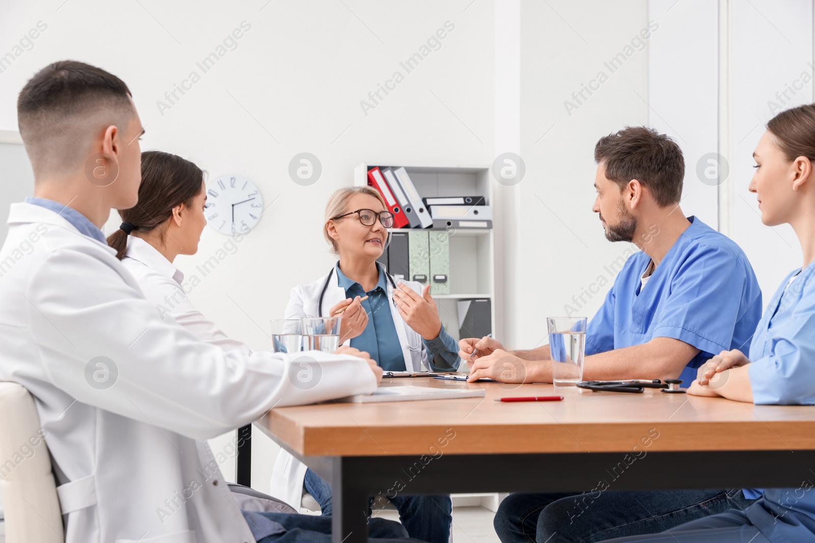 Photo of Medical conference. Team of doctors having discussion with speaker at wooden table in clinic