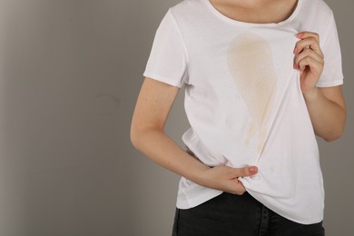 Photo of Woman showing stain from coffee on her shirt against light grey background, closeup. Space for text
