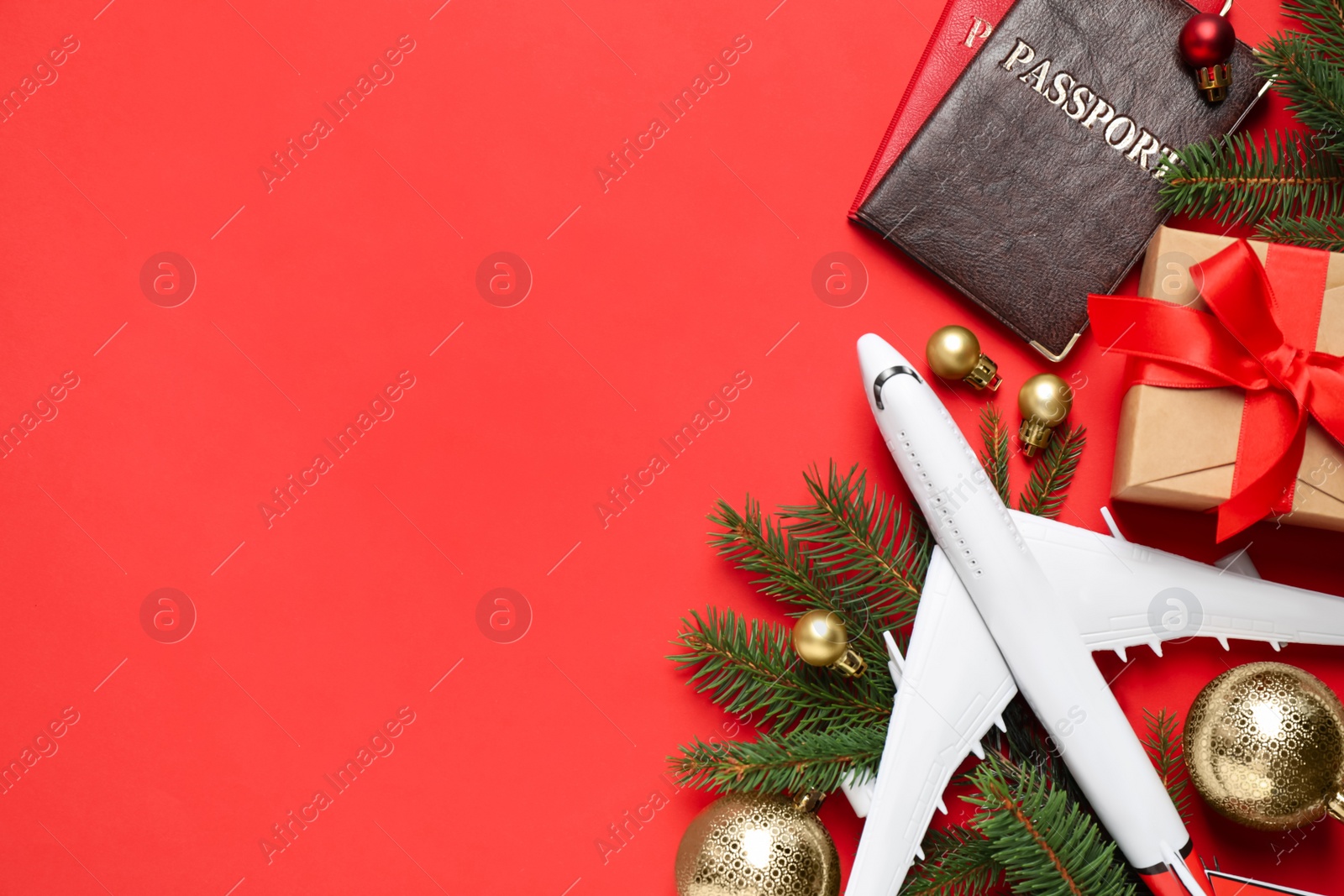 Photo of Flat lay composition with Christmas decorations, toy airplane and passports on red background, space for text. Winter vacation