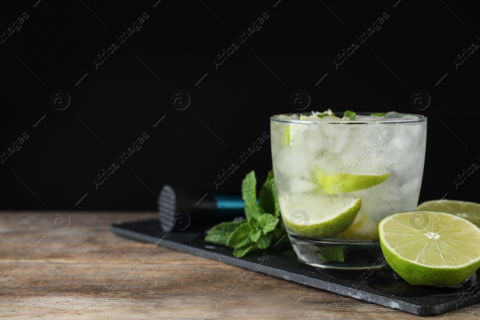 Photo of Glass of cocktail with vodka, ice and lime on wooden table against black background. Space for text