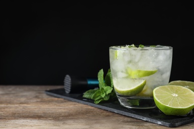 Glass of cocktail with vodka, ice and lime on wooden table against black background. Space for text