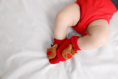 Photo of Baby wearing festive Christmas socks on white bedsheet, closeup. Space for text