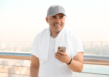 Photo of Handsome mature man in sportswear with mobile phone on bridge. Healthy lifestyle