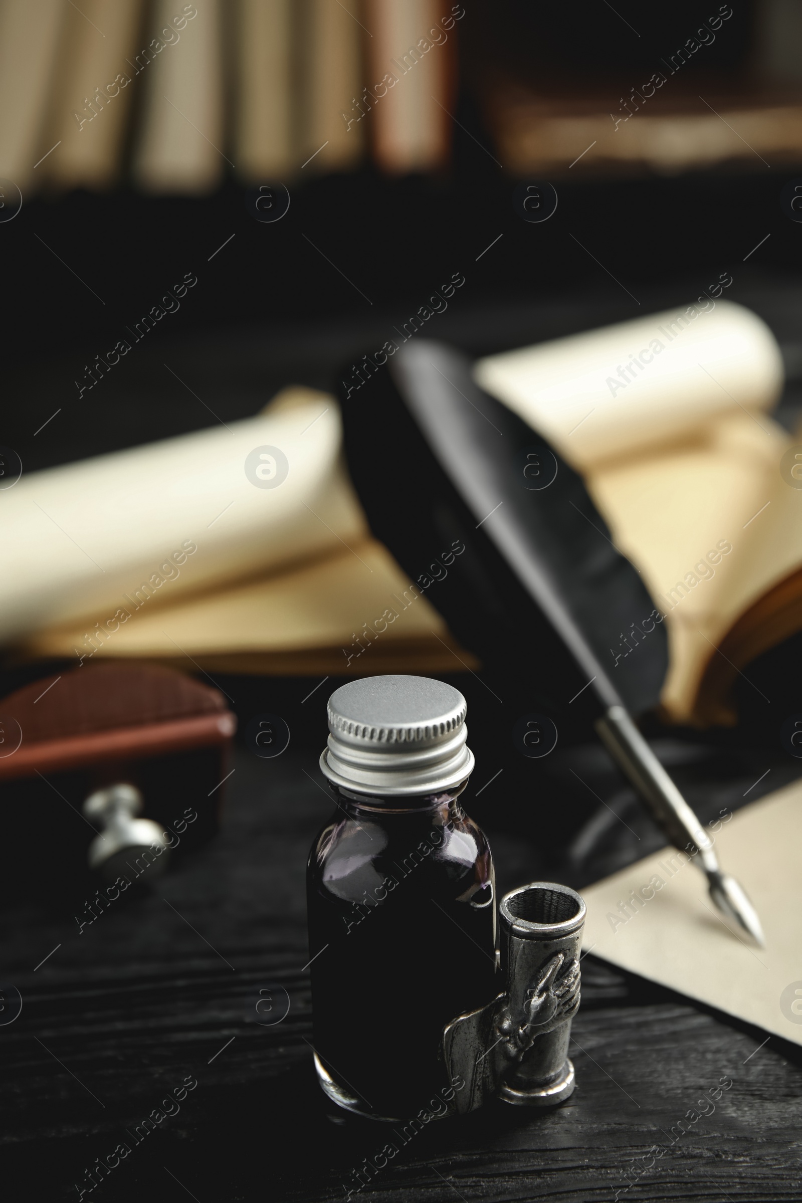 Photo of Feather pen and bottle of ink on black wooden table