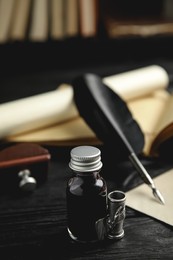 Feather pen and bottle of ink on black wooden table