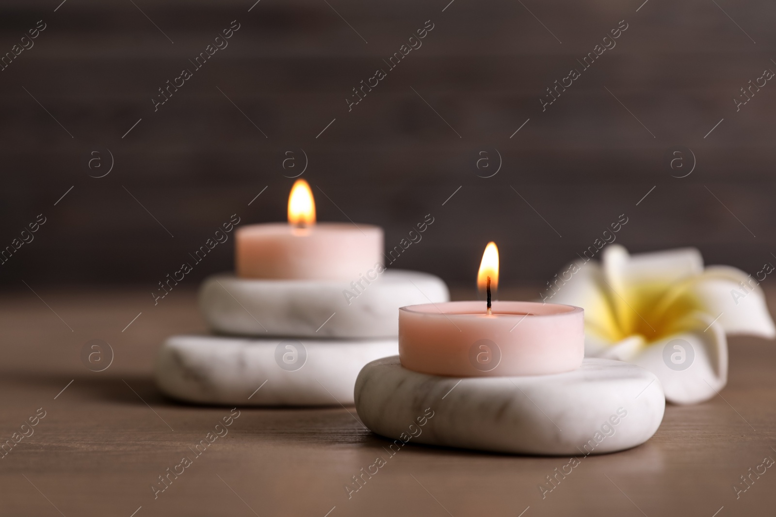 Photo of Composition of spa stones, flower and burning candles on wooden table