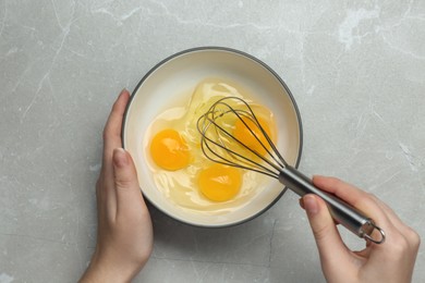 Photo of Woman whisking eggs in bowl at light grey table, top view