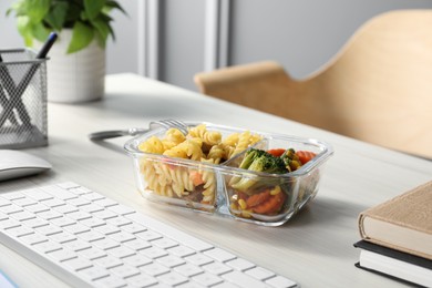 Photo of Container with tasty food, keyboard and books on white wooden table. Business lunch