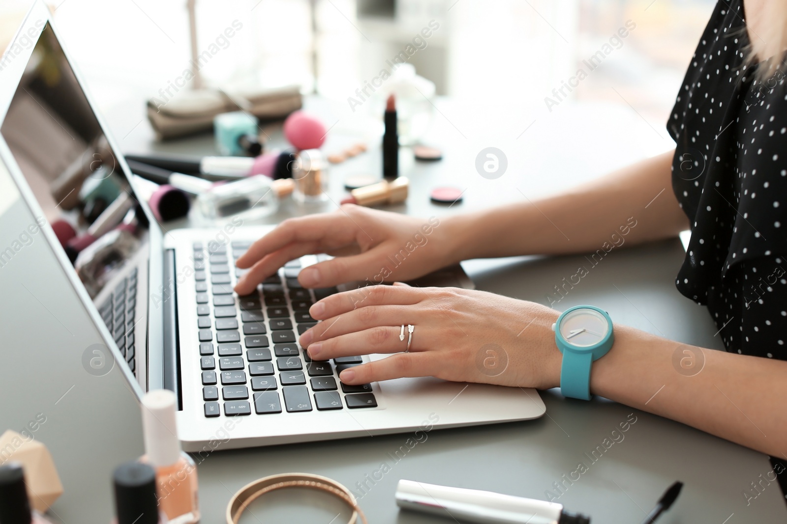 Photo of Young woman with makeup products using laptop at table. Beauty blogger