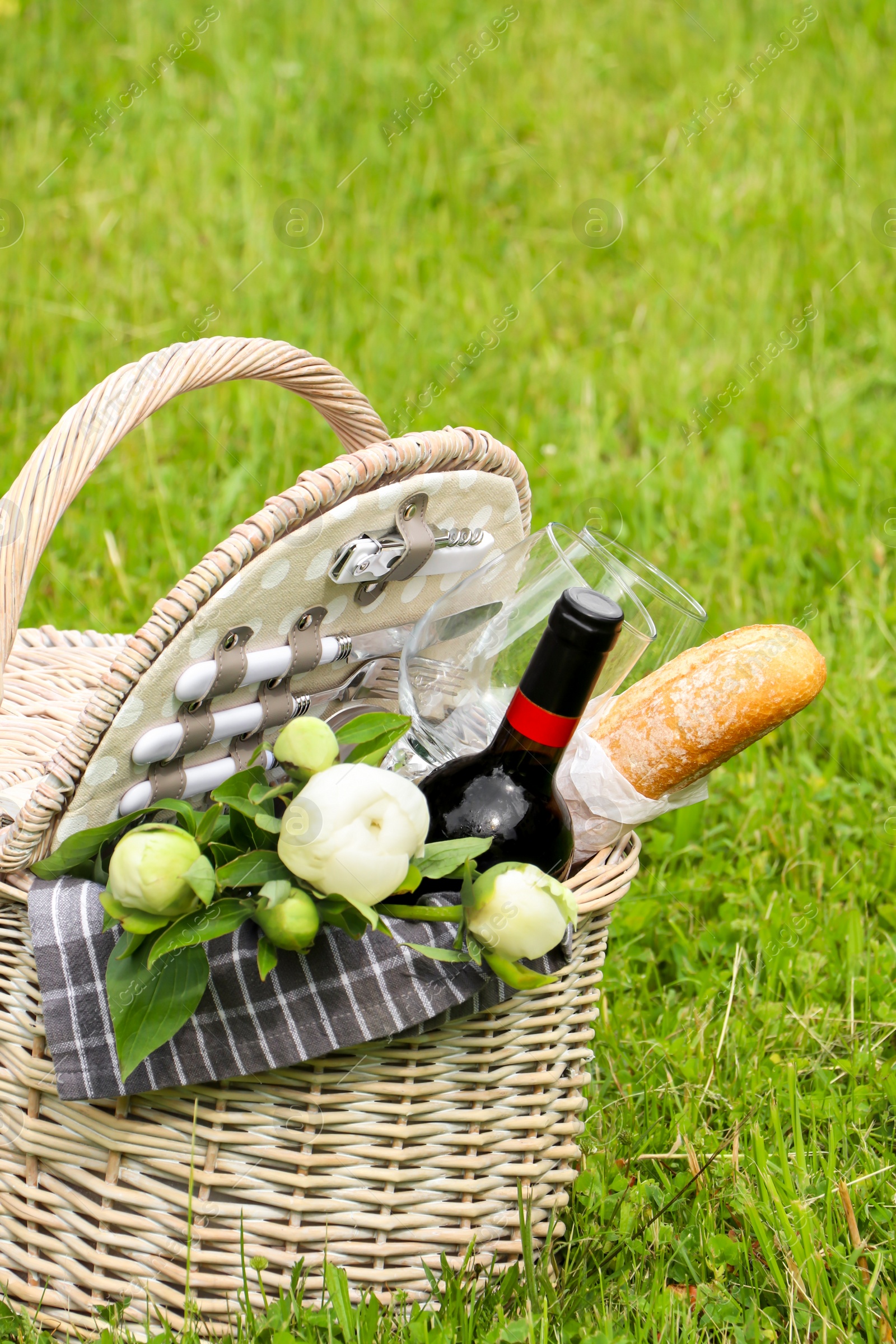 Photo of Picnic basket with wine, bread and flowers on green grass outdoors