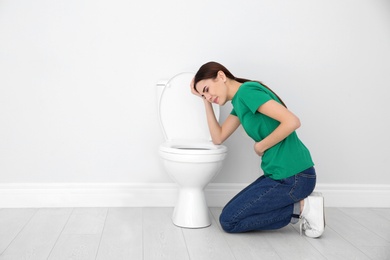 Photo of Young woman suffering from nausea at toilet bowl indoors. Space for text
