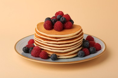 Photo of Stack of tasty pancakes with raspberries and blueberries on pale orange background