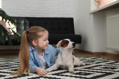 Photo of Cute little girl with her dog on carpet at home. Childhood pet