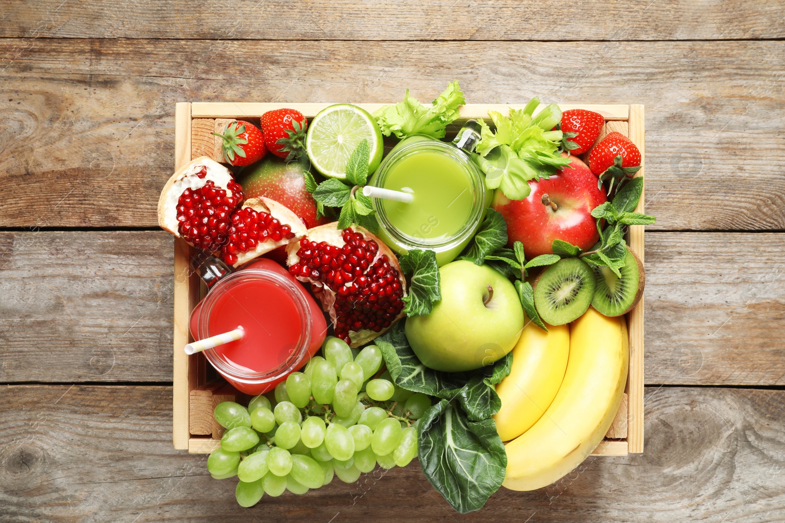 Photo of Wooden crate with juices in mason jars and fresh fruits on wooden background. Top view