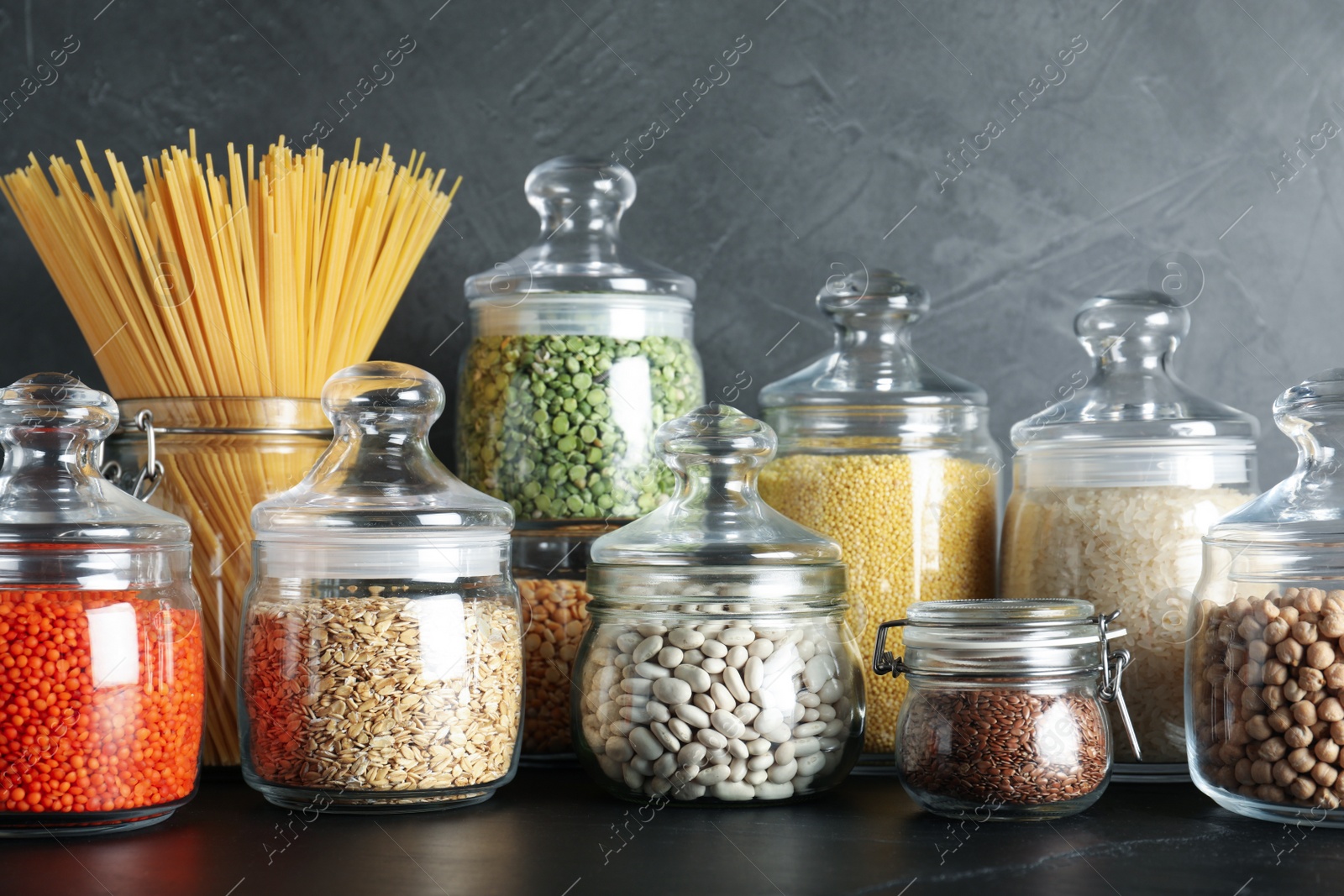 Photo of Glass jars with different types of groats and pasta on black table