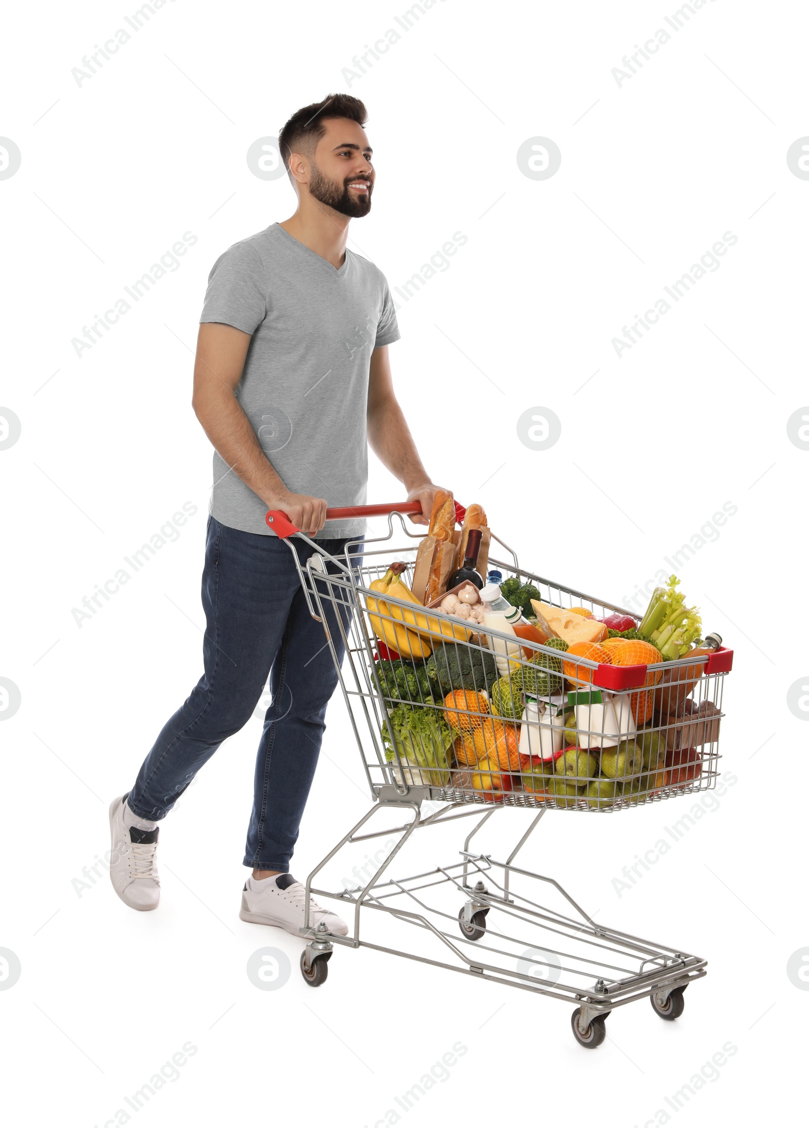 Photo of Happy man with shopping cart full of groceries on white background