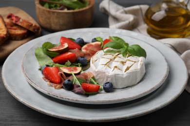 Photo of Delicious salad with brie cheese, prosciutto, figs and strawberries on grey wooden table, closeup