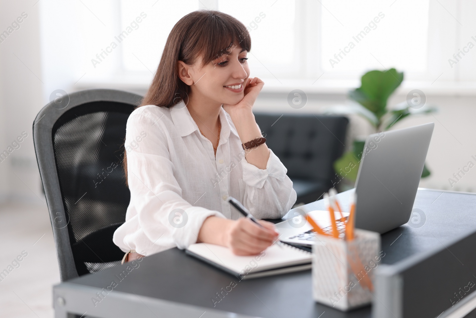 Photo of Woman taking notes during webinar at table indoors
