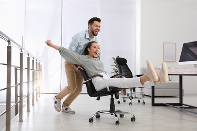 Photo of Office employee giving his colleague ride in chair at workplace