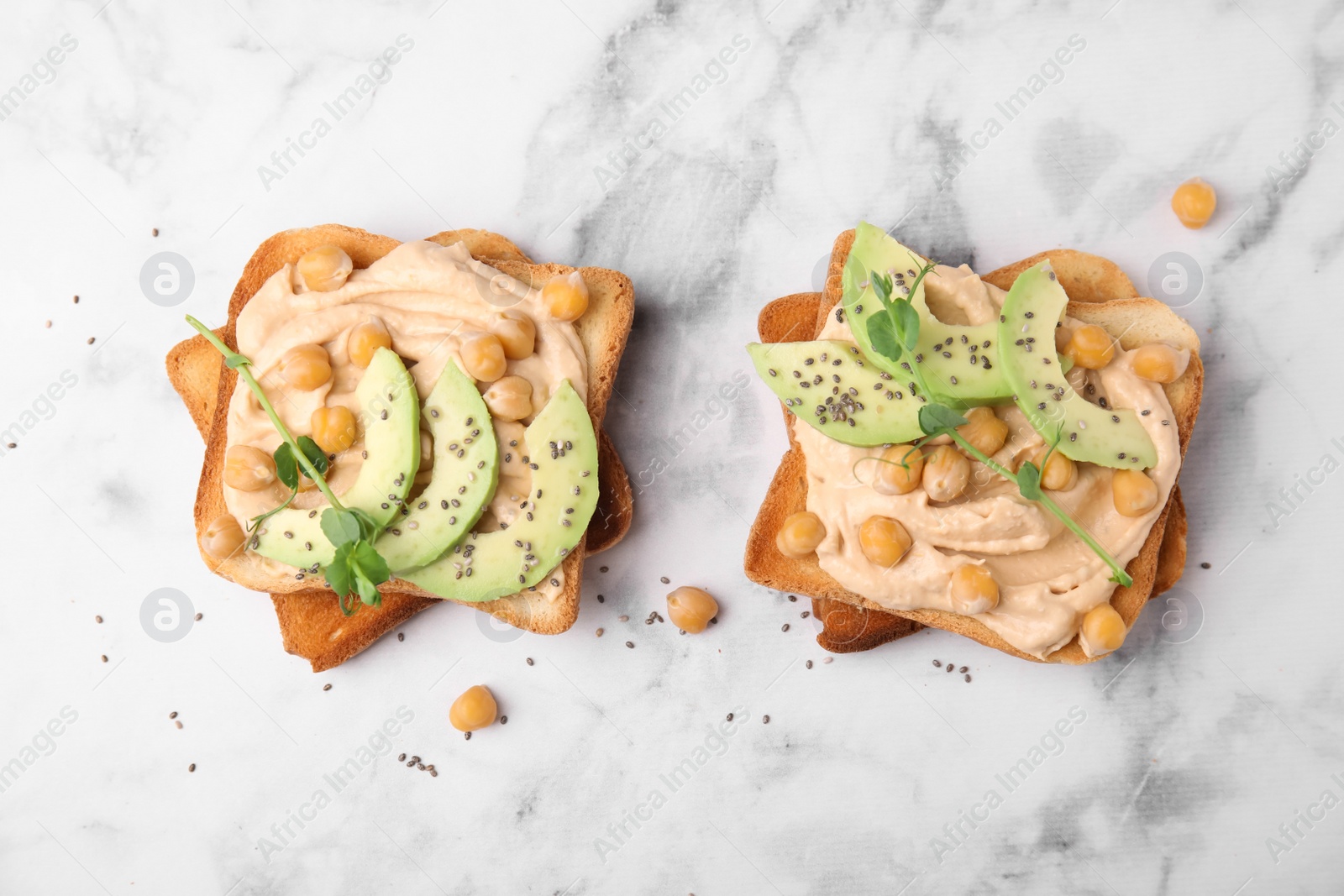 Photo of Delicious sandwiches with hummus, avocado and chickpeas on white marble table, flat lay
