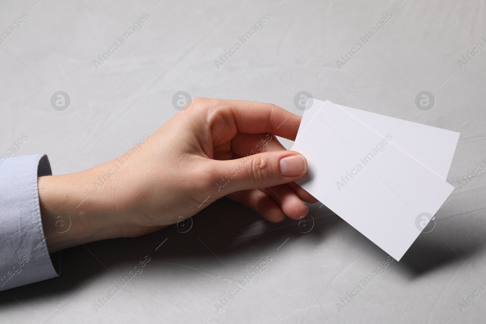 Photo of Woman holding blank cards at light grey table, closeup. Mockup for design