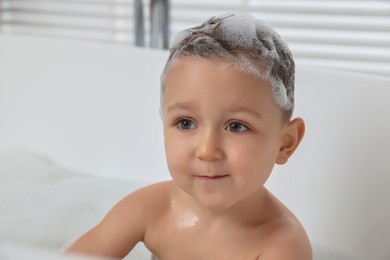 Cute little boy washing hair with shampoo in bathroom