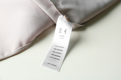 Photo of Clothing label with size and content information on light garment, closeup