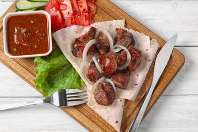 Wooden board with shish kebab and sauce on table, top view