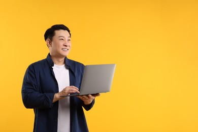Photo of Portrait of happy man with laptop on yellow background. Space for text