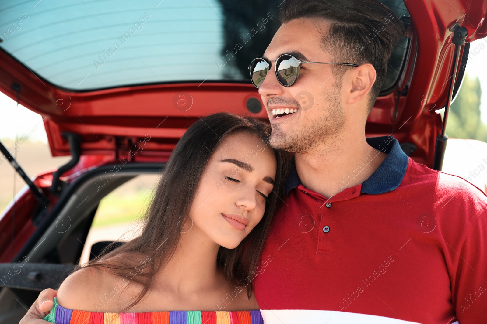 Photo of Happy young couple standing near car in shade