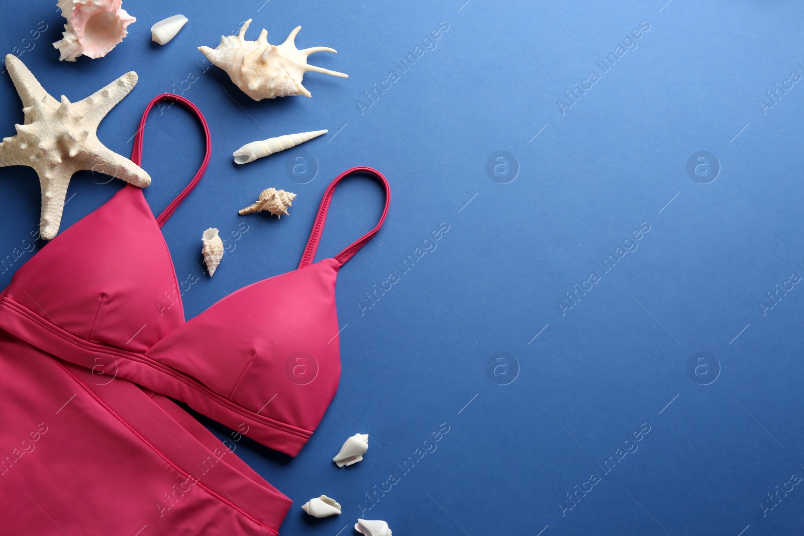 Photo of Beautiful pink bikini and beach accessories on blue  background, flat lay. Space for text