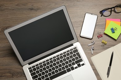 Photo of Modern laptop, smartphone and office stationery on wooden table, flat lay. Distance learning