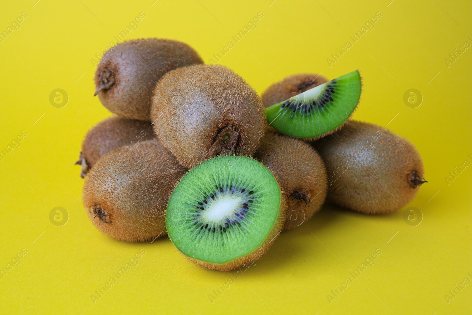 Photo of Heap of whole and cut fresh kiwis on yellow background