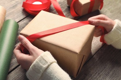 Christmas present. Woman tying ribbon around gift box at wooden table, closeup