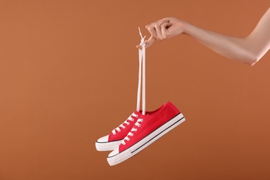 Woman holding pair of red classic old school sneakers on brown background, closeup