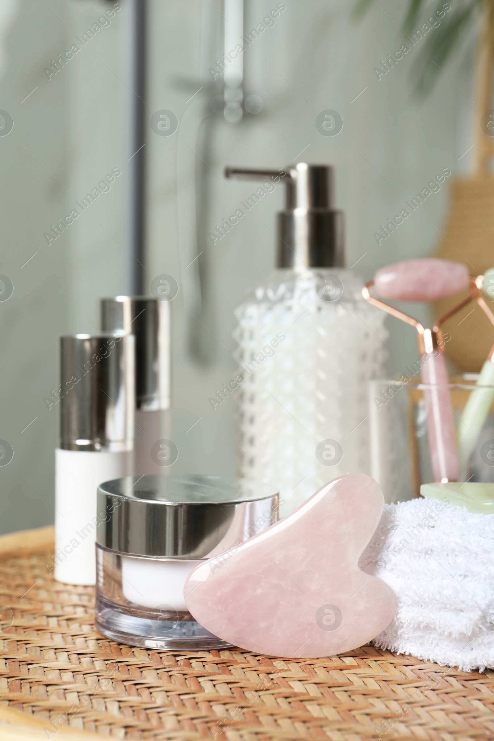 Photo of Rose quartz gua sha tool, natural face rollers and toiletries on wicker table indoors