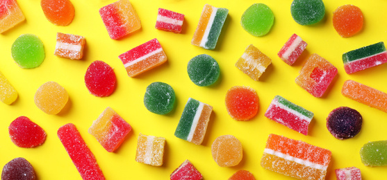 Flat lay composition with delicious colorful candies on yellow background. Banner design 