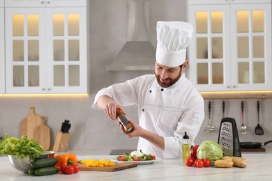 Photo of Professional chef adding pepper into delicious salad at marble table in kitchen