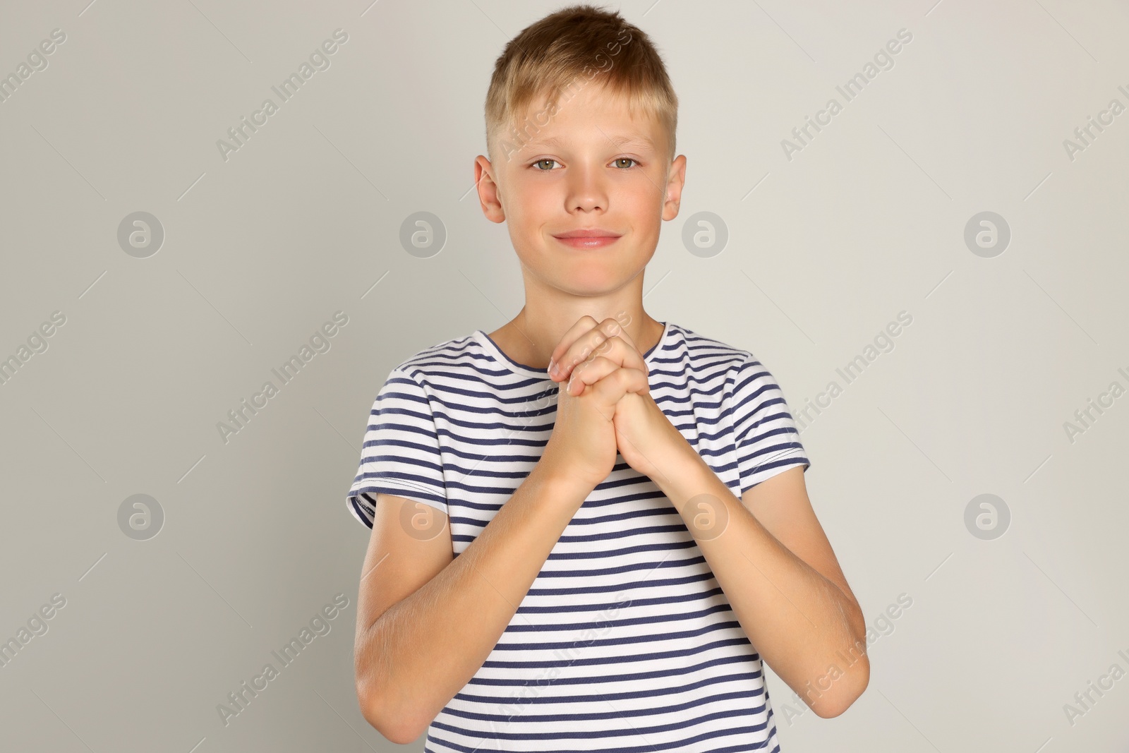 Photo of Boy with clasped hands praying on light grey background