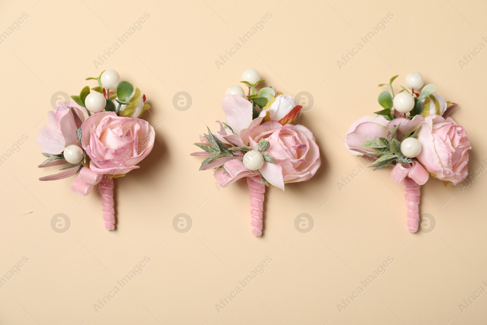 Photo of Stylish pink boutonnieres on beige background, flat lay