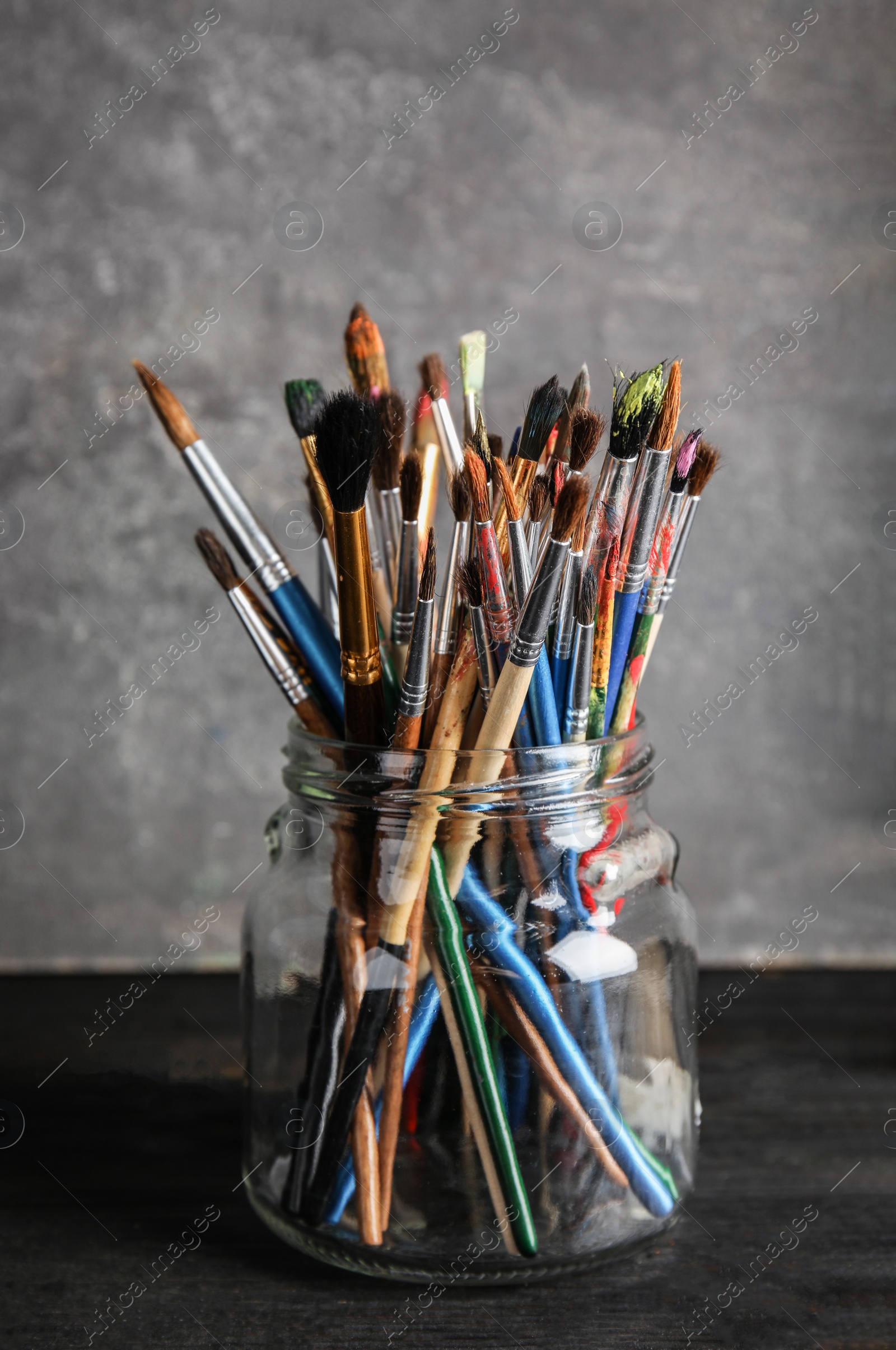 Photo of Jar with paint brushes on table against grey background