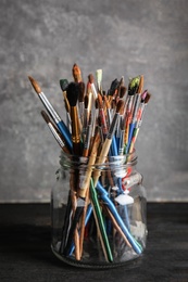 Jar with paint brushes on table against grey background