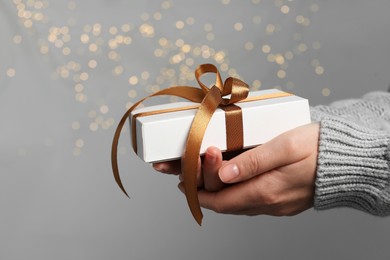 Photo of Christmas present. Woman holding gift box against grey background with blurred lights, closeup. Space for text