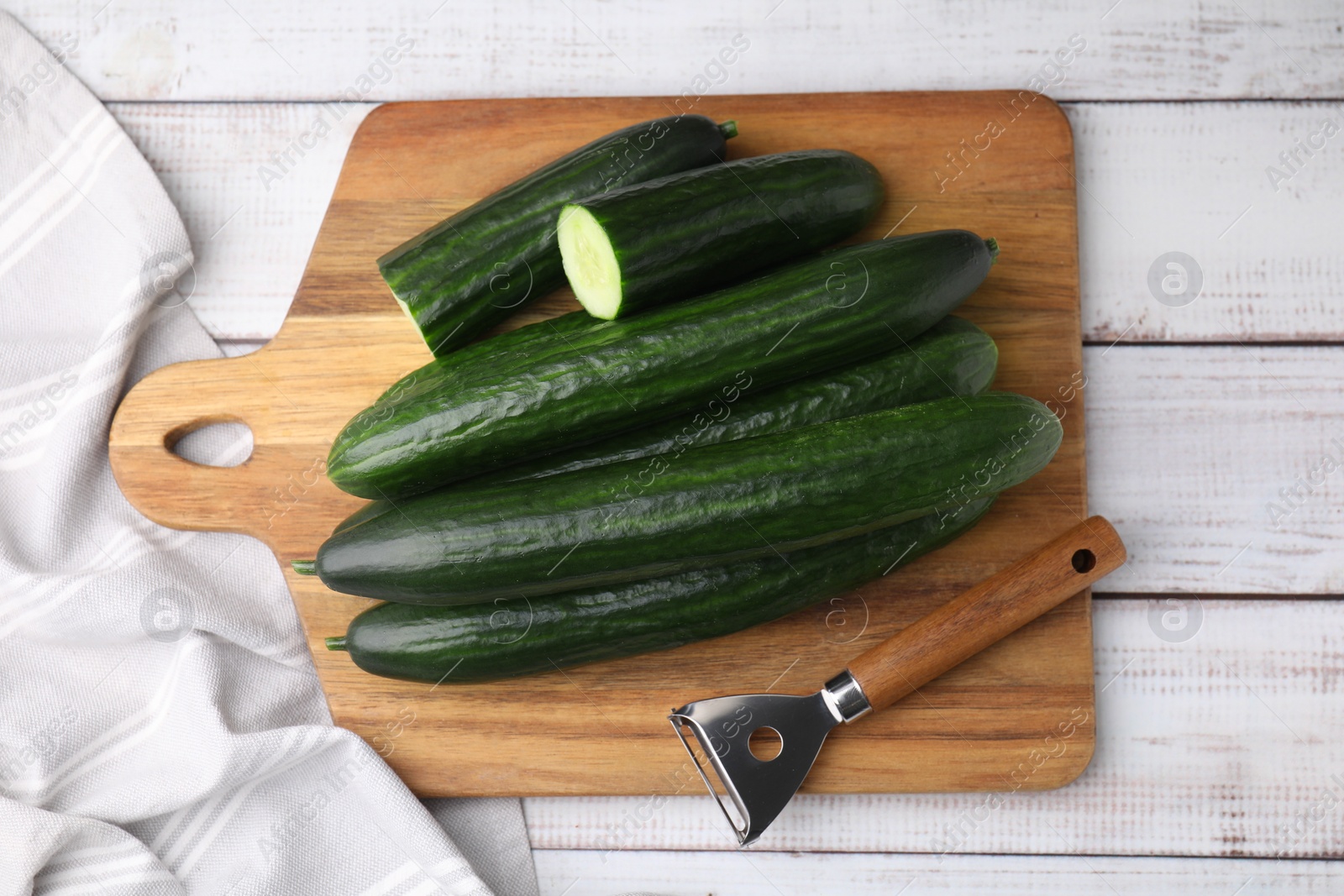 Photo of Fresh cucumbers and peeler on white wooden table, top view