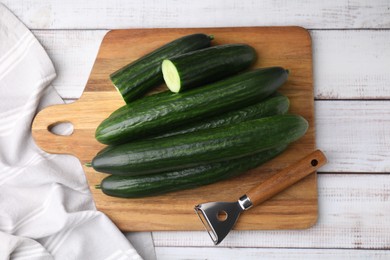 Fresh cucumbers and peeler on white wooden table, top view