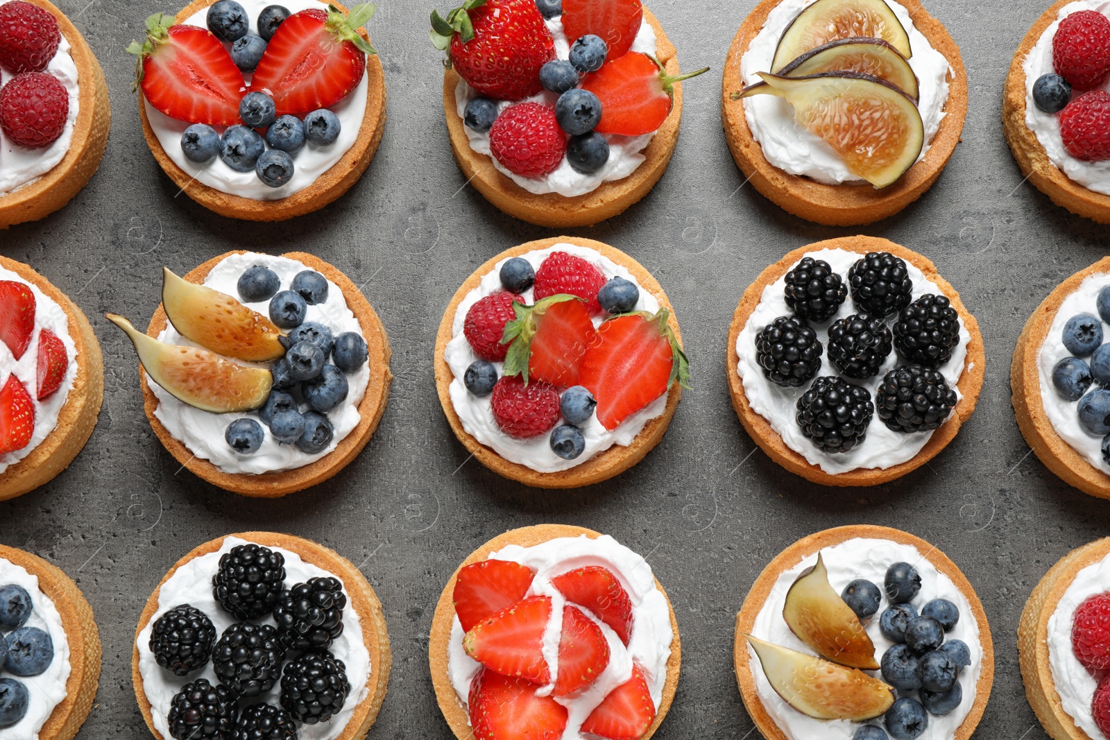 Photo of Different berry tarts on grey table, flat lay. Delicious pastries