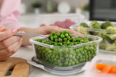 Photo of Woman taking green peas with spoon from glass container at table in kitchen, closeup. Food storage