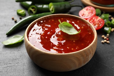 Photo of Spicy chili sauce with basil in bowl on black table, closeup