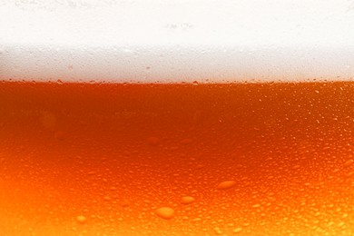 Photo of Glass of tasty cold beer with foam and condensation drops, closeup