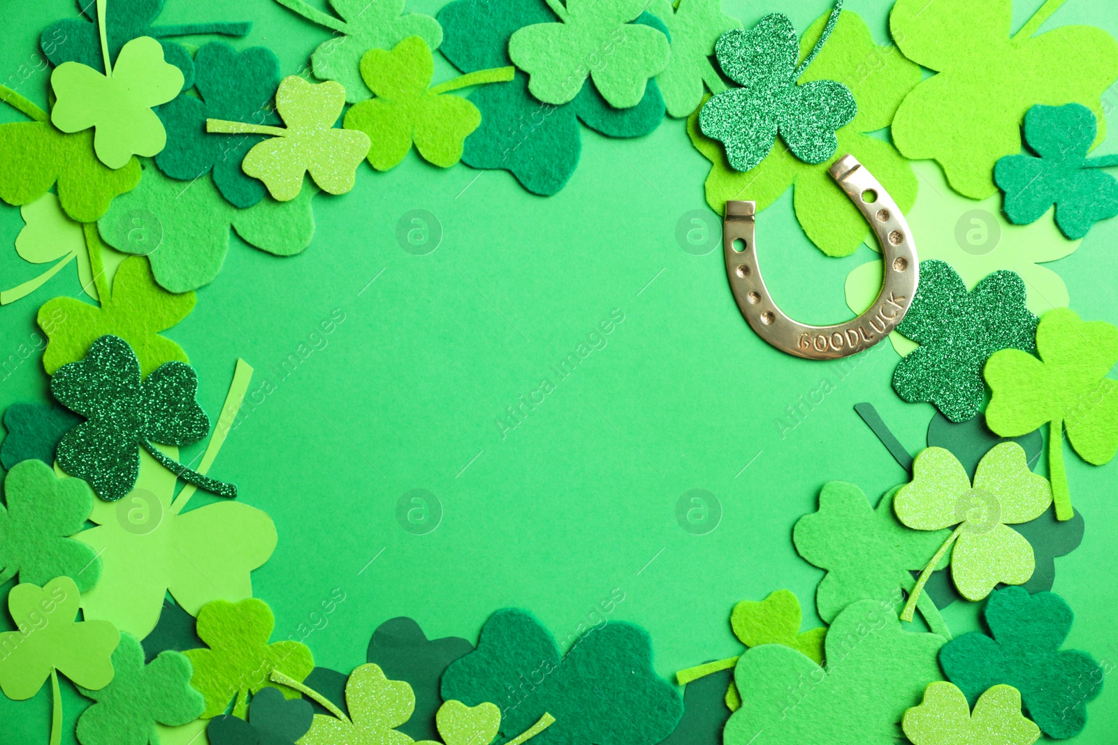 Photo of Frame made of clover leaves and horseshoe on green background, flat lay with space for text. St. Patrick's day